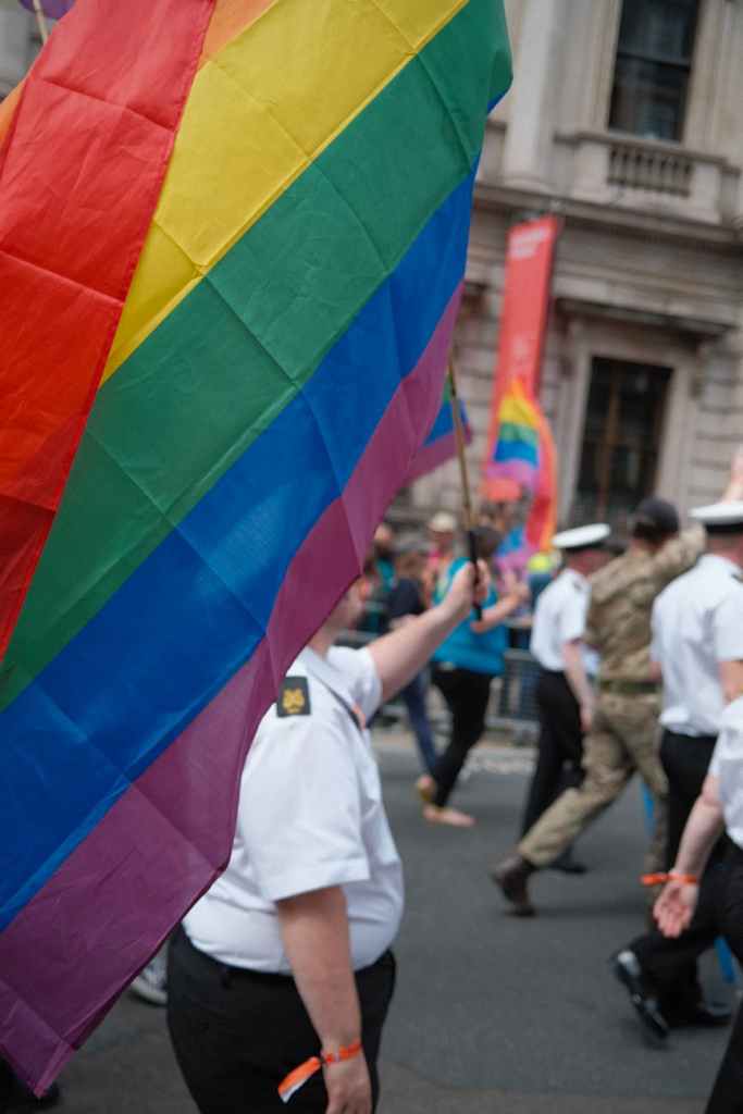 person in military uniform waving a rainbow flag
